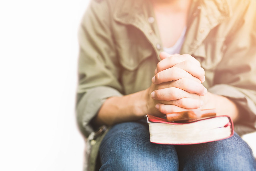 man praying on holy bible in the morning.teenager boy hand with Bible praying,Hands folded in prayer on a Holy Bible in church concept for faith, spirituality and religion