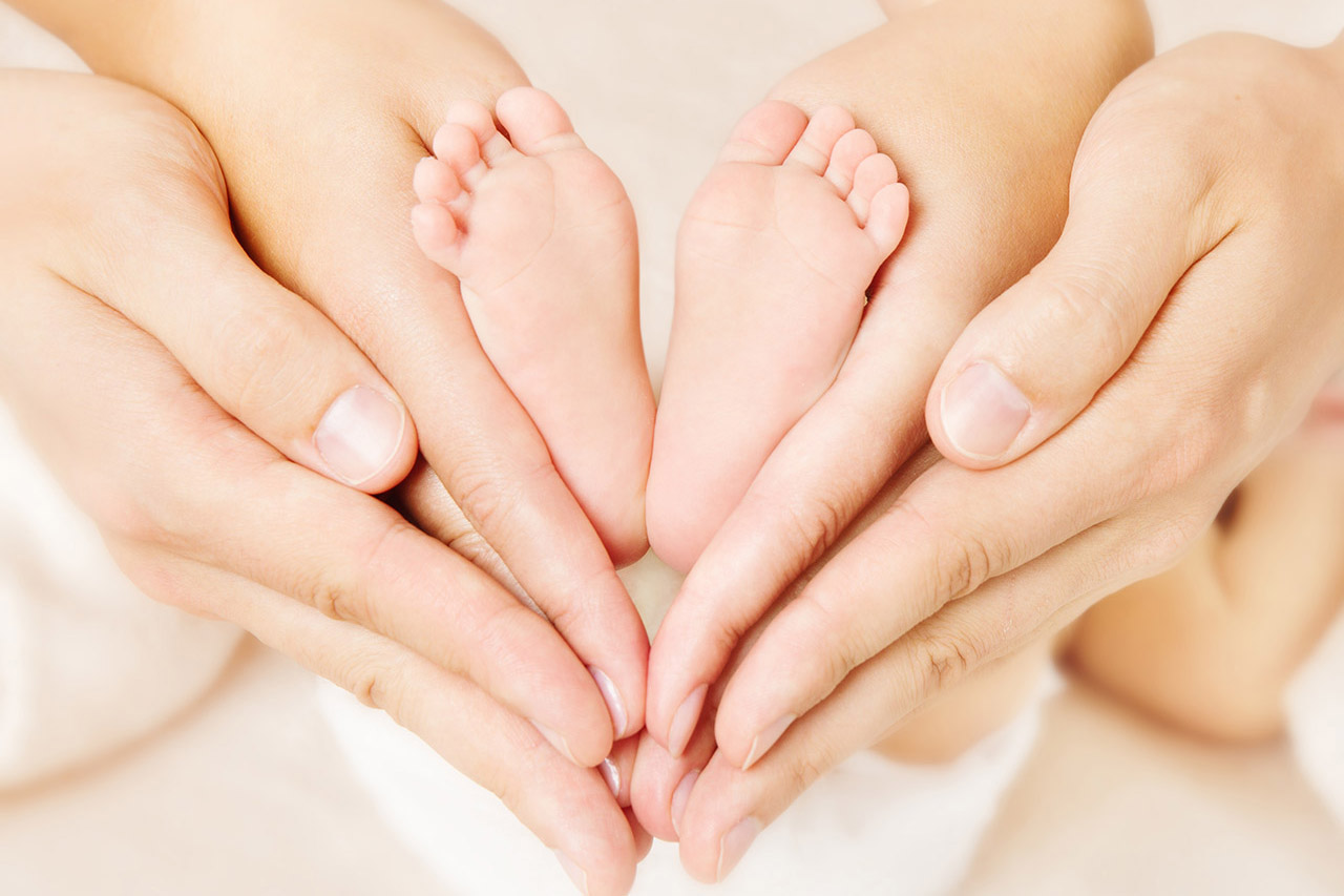 Newborn baby feet parents holding in hands. Love simbol as heart sign.